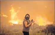  ??  ?? A woman watches as the Bobcat Fire burns Friday in Juniper Hill, Calif. [RINGO H.W. CHIU/ THE ASSOCIATED PRESS]