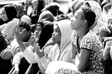  ?? — Reuters photo ?? African migrants gesture as they sit in a detention camp in Tripoli, Libya.