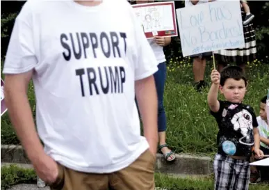  ?? STAFF PHOTOS BY DOUG STRICKLAND ?? Dominic Banks, right, holds a sign Saturday as Allen Gillespie stands nearby wearing a “Support Trump” T-shirt during a demonstrat­ion in the parking lot of Delray Farms Fresh Market in Dalton, Ga. Dozens of demonstrat­ors gathered to protest the detention and separation of immigrant families at the United States border.