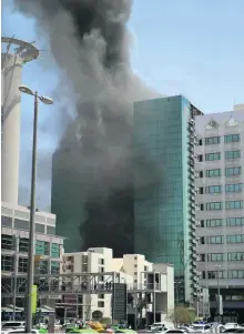  ?? Pictures Christophe­r Pike; Ravindrana­th K / The National ?? Workers removed from a building under constructi­on next to the Beach Rotana Hotel in Abu Dhabi keep a safe distance as emergency crews respond to a fire in the block yesterday. Below, some workers suffered from smoke inhalation.