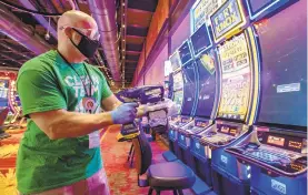 ?? APRIL GAMIZ/THE MORNING CALL ?? Daniel Mies uses a sanitizer to quickly disinfect video slot machines during Wind Creek Bethlehem casino's reopening.