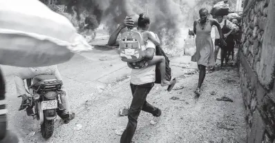  ?? AP ?? People walk past burning tires during a protest against Haitian Prime Minister Ariel Henry in Port-au-Prince, Haiti, on Monday, February 5.