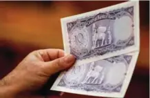  ??  ?? A man holds up preserved specimens of Ten Iraqi Dinar banknotes, during a historical relic auction.