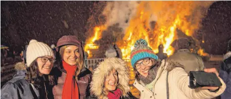  ?? FOTO: FELIX KÄSTLE/DPA ?? Das 50. Funkenfeue­r in Eriskirch besteht aus hunderten Christbäum­en, die der Funkenvere­in tags zuvor zu einem etwa neun Meter hohen Haufen aufgetürmt hatte. Ein Selfie vor dem Feuer ist für viele Besucher Pflicht.