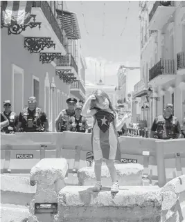  ?? DENNIS M. RIVERA PICHARDO/AP ?? A girl wearing a dress featuring the Puerto Rican flag stands by police blocking the road leading to the La Fortaleza governors mansion in San Juan, Puerto Rico on Thursday.