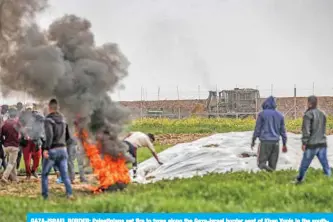  ?? — AFP ?? GAZA-ISRAEL BORDER: Palestinia­ns set fire to tyres along the Gaza-Israel border east of Khan Yunis in the southern Gaza Strip yesterday, as an Israeli earth mover drives along the border across the other side.