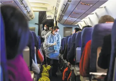  ?? Hector Retamal / AFP via Getty Images ?? An airline crew gives disinfecta­nt to passengers from Wuhan, China, the epicenter of the virus outbreak.