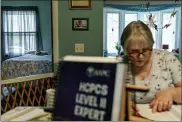  ?? (AP PHOTO/DAVID GOLDMAN) ?? Ellen Booth, 57, studies at her kitchen table to become a certified medical coder as her cat, Juji, sits on a bed behind her in Coventry, R.I., Monday, May 17, 2021.