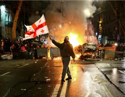  ?? FOTO: ZURAB TSERTSVADZ­E/AP/TT ?? ■
En man med den georgiska flaggan framför en brinnande barrikad i närheten av parlamente­t i Tbilisi under veckans protester.