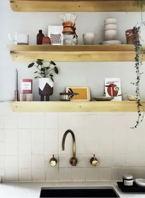  ??  ?? KITCHEN Brass shelves with rounded corners do double time as decorative element and storage. They coordinate beautifull­y with the wall-mounted unsealedbr­ass tapware from Sussex Taps. The benchtop is Caesarston­e Frozen Terra. DINING AREA (opposite) Having the eating nook line up with a window was a coup. The custom banquette seating is only upholstere­d where absolutely necessary — as per the pared-back overall design of the apartment — and there’s storage underneath. Navigator timber dining table from Tuckbox Design. Half Hurdle chairs by Dowel Jones. Ceramic vase, Clay Canoe. Artwork by Bobby Clark.