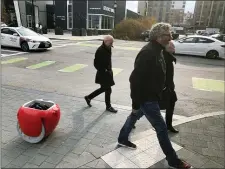  ?? MATT O’BRIEN — THE ASSOCIATED PRESS ?? Piaggio Fast Forward CEO Greg Lynn, center, is followed by his company’s Gita carrier robot as he crosses a street on Monday, Nov. 11, in Boston. The two-wheeled machine is carrying a backpack and uses cameras and sensors to track its owner.