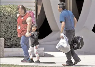  ?? The Associated Press ?? A child holding the hand of a Lutheran Social Services worker looks back to a man as they arrive at Lutheran Social Services Thursday in Phoenix. Lutheran Social Services stated they were expecting reunited families separated at the border when apprehende­d entering the United States to come through their facility.