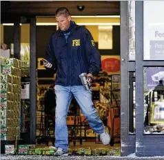  ?? MARK HUMPHREY/AP ?? An FBI agent steps over soft drink bottles and broken glass Friday at a damaged entrance at the Kroger grocery store in Colliervil­le, Tenn., where a gunman killed one person and wounded 14 others.