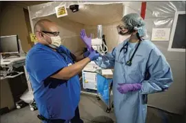  ?? DR. LISA DABBY, Al Seib Los Angeles Times ?? right, is assisted by technician Jorge Velasco in donning personal protective equipment last year at UCLA Medical Center in Santa Monica.