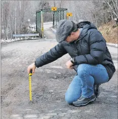  ?? CAROLE MORRIS-UNDERHILL ?? Joe Britten checks to see how big one of the potholes on Bog Road is.