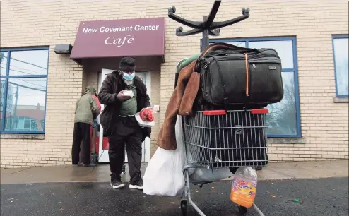  ?? Christian Abraham / Hearst Connecticu­t Media ?? Local David Bond grabs a take-out Christmas dinner in front of New Covenant Cafe in Stamford on Friday. Volunteers from Temple Sinai helped prepare the dinners. The dinner is usually a sit-down service but the pandemic caused the annual event to be take-out only.