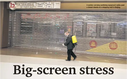  ??  ?? A worker carrying sanitising equipment walks past a closed cinema ata shopping mall in Beijing.