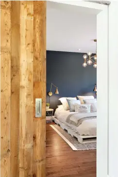  ??  ?? Une porte coulissant­e en bois massif montée sur rail permet d'accéder à la chambre sans perdre de l'espace, en plus d'ajouter de la chaleur et un cachet particulie­r au décor.