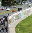  ??  ?? Ein kleines Stück der Mauer, die einst Berlin teilte, steht noch heute. Millionen Touristen kommen jedes Jahr dorthin, um sich die Mauer anzusehen.