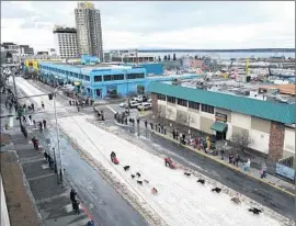  ?? Bill Roth Alaska Dispatch News ?? DAYS BEFORE the race, mushers drive their dog teams down a ribbon of snow placed in an otherwise snow- free downtown Anchorage for the annual Fur Rondy.