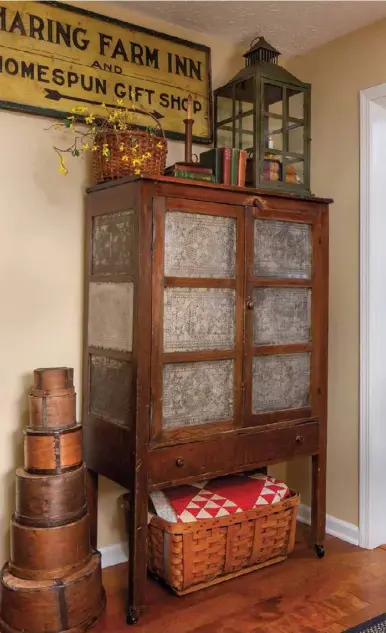  ??  ?? Below: An heirloom pie safe and a sign Sonna picked up at a garage sale add interest to a corner of the dining room. “I saw the sign and literally went running,” she remembers. A green metal lantern fills space atop the pie safe and picks up on some of the hues in the sign, while a vivid red-and-white quilt tucked into a basket beneath commands attention at floor level.