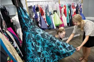  ?? Staff photo by Evan Lewis ?? Lauren Willis holds the dress flat as Brittni Coats steams a prom dress Tuesday at Traditions Bridal and Formal. The longtime dress boutique is under new ownership and has expanded its dress lines and now offers more contempora­ry dress designers.