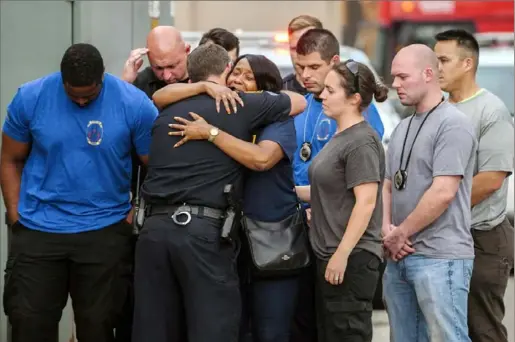  ?? Alexandra Wimley/ Post- Gazette ?? Mourners of Pittsburgh police Officer Calvin Hall, who died Wednesday after being shot Sunday, gather outside the Allegheny County medical examiner's office in the Strip District following a procession of police vehicles from UPMC Presbyteri­an. Sgt. Joseph Lewis, who heads the Northview Heights Public Safety Center, hugs an unidentifi­ed woman. Officer Hall was shot while off duty in Homewood.