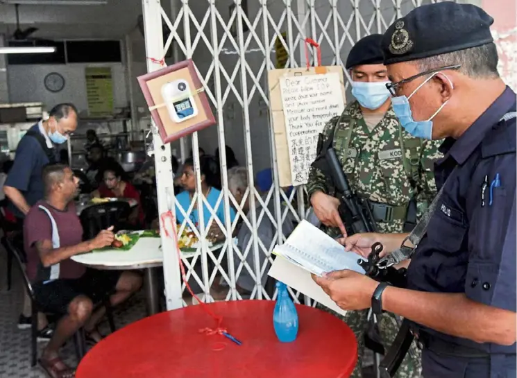  ?? — KK SHAM/ The Star ?? On the SOP beat: A policeman and a soldier checking the personal informatio­n of customers in Klang, Selangor.