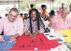  ?? CONTRIBUTE­D ?? Opposition Leader and People’s National Party (PNP) President Dr Peter Phillips (right) paints a message on a T-shirt at the Mary Seacole Hall T-Shirt project in recognitio­n of Internatio­nal Day for the Eliminatio­n of Violence Against Women at The University of the West Indies on Thursday. Also involved in the project are first vice-president of the PNP Senator Damion Crawford (centre) and Shadow Minister for Transport Mikael Phillips.