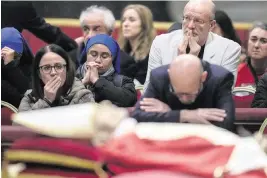  ?? ALESSANDRA TARANTINO AP ?? Mourners pray in front of the body of late Pope Emeritus Benedict XVI, his head resting on a pair of crimson pillows, in St. Peter’s Basilica at The Vatican on Wednesday. Thousands of people filed by to pay tribute to the pontiff who shocked the world by retiring a decade ago. Benedict died Saturday at the age of 95. His funeral is planned for Thursday.