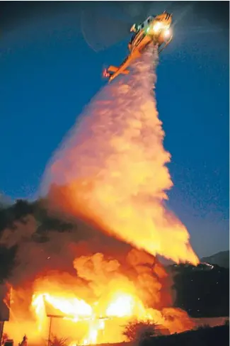  ?? Photo: REUTERS ?? Towns threatened: A helicopter makes a water drop on a garage consumed by a wildfire raging out of control in the high desert east of Los Angeles.