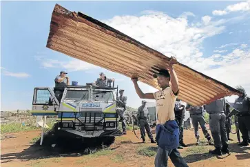  ?? /HALDEN KROG ?? A resident of the Itireleng informal settlement, west of Pretoria, carries roof sheets salvaged from his demolished shack. The City of Tshwane metro police have overspent on preventing illegal land invasions.
