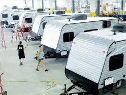  ?? (Joshua Lott/Reuters) ?? WORKERS WALK around single-axle towable Pioneer traditiona­l recreation­al vehicles at the Thor Industries Heartland RV assembly plant in Elkhart, Indiana, earlier this year.