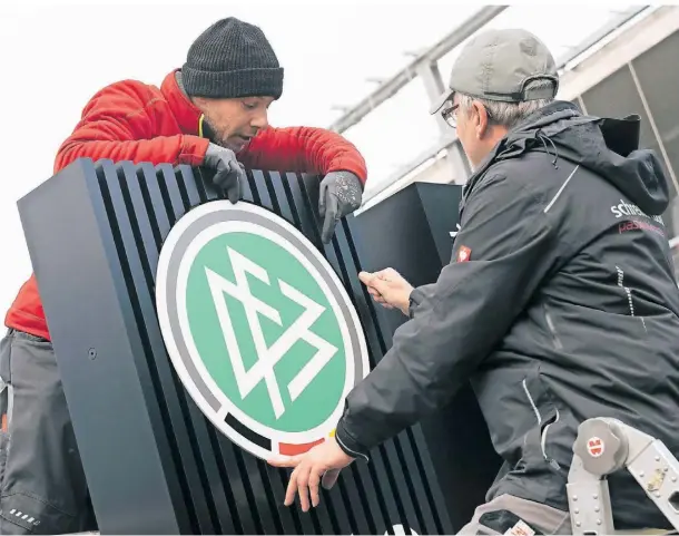  ?? FOTO: BORIS ROESSLER/DPA ?? Zwei Arbeiter montieren am 7. Dezember das DFB-Logo am Verbands-Campus in Frankfurt.