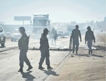  ?? Picture: Jacques Nelles ?? CROSSFIRE. Police officers are seen walking along the N14 highway near Diepsloot, Johannesbu­rg, where residents blocked the roads and highway during a service delivery protest yesterday.
