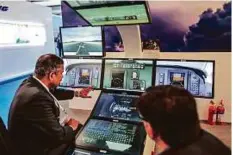  ?? Bloomberg ?? An employee (left) shows a simulation system at the Rockwell Collins booth during the Aero India air show last year. Rockwell’s investment­s are geared towards the smart plane era.