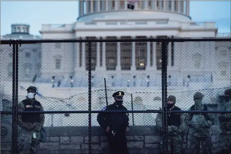  ?? Brendan Smialowski I / AFP via Getty Images ?? A Capitol Police officer stands with members of the National Guard behind a crowd-control fence surroundin­g Capitol Hill on Thursday.