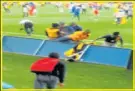  ??  ?? FATAL SHOT: The police officer, now back on his feet, is seen between two fans as others continue to invade the field. The shooting victim, Ntandazo Mbenje, is seen in a yellow shirt falling back over the advertisin­g board, fractions of a second later