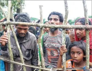  ?? SAM JAHAN/FP ?? Rohingya refugees stand behind a fence at Kutupalong refugee camp in Ukhiya after crossing the border from Myanmar into Bangladesh on Tuesday.