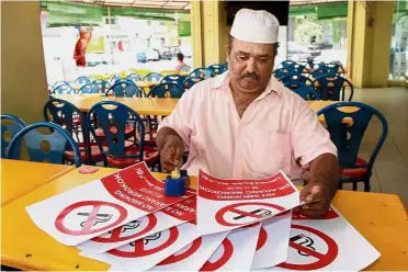  ??  ?? In four languages: Restoran Alif Maju owner Abbas Abu Bakar preparing ‘no smoking’ signs for his outlet in Klang.