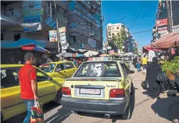  ??  ?? A taxi with an image of President Bashar Assad on the back window drives along a busy street with stalls in Aleppo. His image is everywhere throughout Syria.