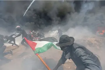  ?? — Reuters photo ?? Palestinia­n demonstrat­ors run for cover from Israeli fire and tear gas during a protest against US embassy move to Jerusalem and ahead of the 70th anniversar­y of Nakba, at the Israel-Gaza border in the southern Gaza Strip.