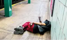 ?? — AFP photos ?? A homeless man smokes a cigarette while lying on the ground in a subway station in Manhattan, New York on.