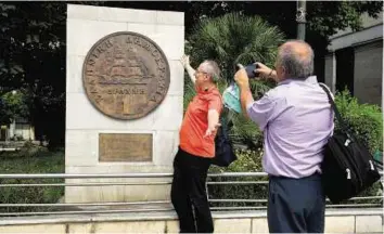  ?? AP ?? Old money A man poses for a picture in front of a plaque in Athens of a Greek one-drachma coin, which was replaced by the euro in 2002.