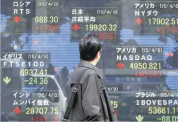  ?? — Reuters ?? A pedestrian looks at an electronic board showing the stock market indices outside a brokerage in Tokyo.