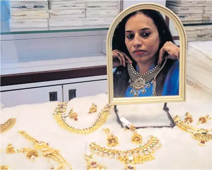  ?? REUTERS ?? A woman tries on a gold necklace inside a jewellery showroom at a market in Mumbai. Indian jewellery firms are finding it increasing­ly hard to get credit to import raw material and ship out their wares as banks tighten the screws, worried about...