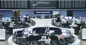  ?? — Reuters ?? Traders work at their desks in front of the German share price index, DAX board, at the stock exchange in Frankfurt.