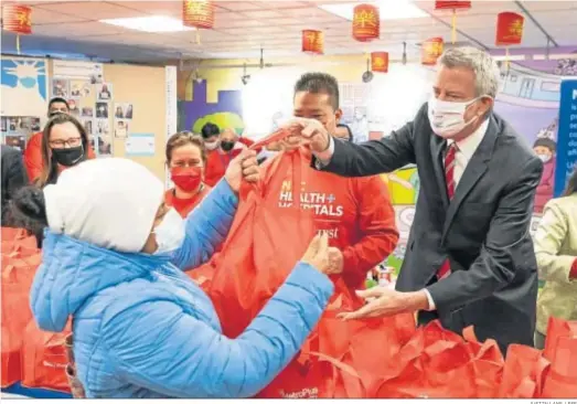  ?? JUSTIN LANE / EFE ?? El alcalde de Nueva York, Bill de Blasio, reparte bolsas con comida a los afectados por la crisis en un centro hospitalar­io de Queens.