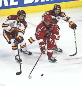  ?? GETTY IMAGES ?? Harvard's Tyler Moy moves the puck between a pair of Minnesota-Duluth players during the Crimson’s loss to the Bulldogs in an NCAA semifinal last April at the United Center in Chicago.