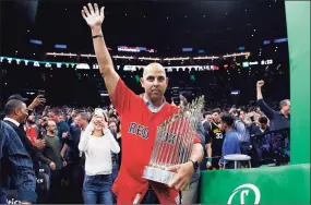  ?? Michael Dwyer / Associated Press ?? Boston Red Sox manager Alex Cora waves as he walks onto the court with the baseball World Series trophy during the first half of an NBA basketball game between the Boston Celtics and the Milwaukee Bucks in Boston on Nov. 1, 2018. The Red Sox rehired Cora as manager on Friday, less than a year after letting him go because of his role in the Houston Astros cheating scandal.